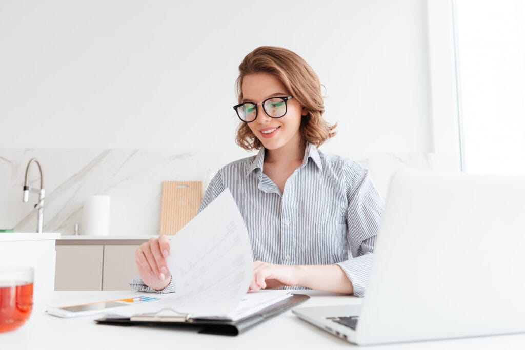 Cheerful woman in glasses reading new contract while working in the kitchen